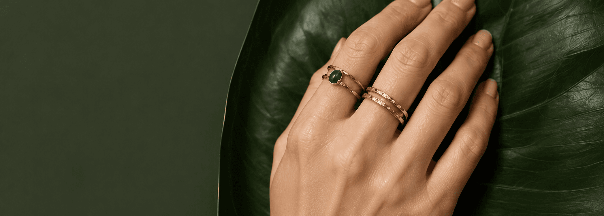 A hand wearing stacked rings resting on a green leaf