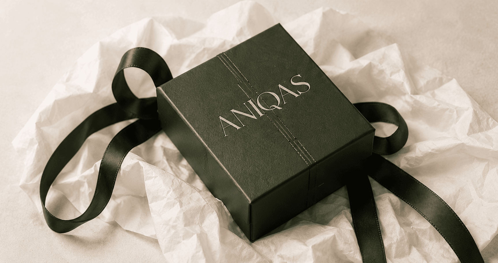 A green ANIQAS jewellery gift box with ribbon on cream fabric